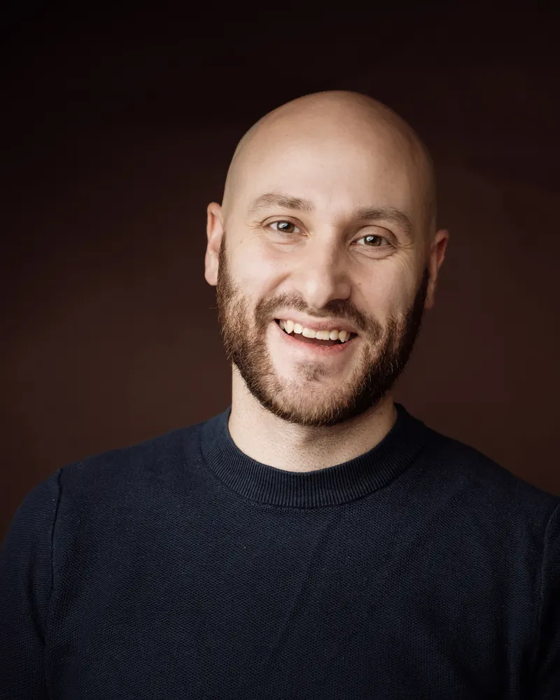 Portrait d’Armen, photographe, souriant sur fond sombre