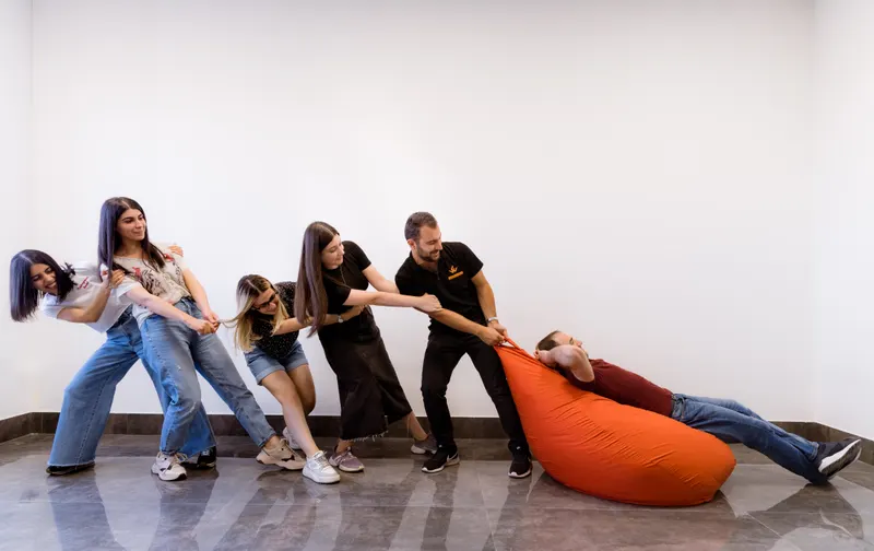 Jeu d’équipe : des collègues tirent un pouf orange, rires et mouvement