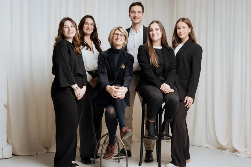 Six collaborateurs posant ensemble en tenue sombre et blanche, devant un rideau clair