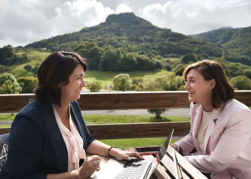 Deux collègues éclatent de rire sur une terrasse, montagne en arrière-plan