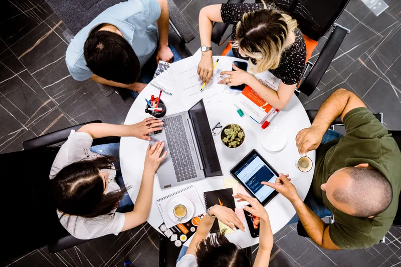 Cinq collègues autour d’une table avec ordinateur et tablette, vue du dessus