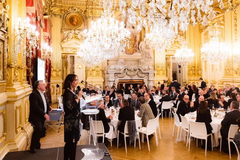 Discours d’une oratrice lors d’un dîner, salle dorée et convives assis