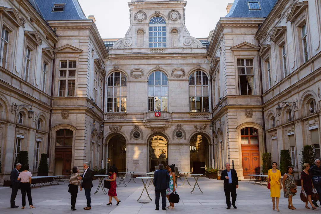 Cocktail dans la cour d’un bâtiment historique, invités debout autour de tables hautes