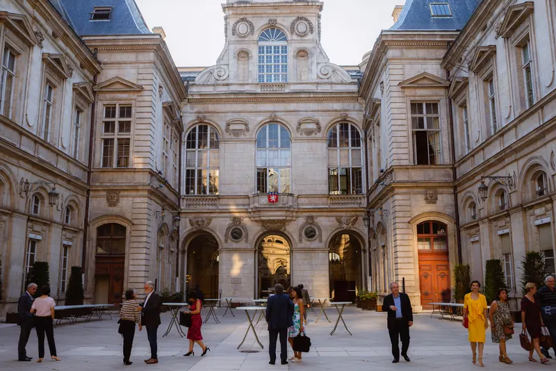 Cocktail dans la cour d’un bâtiment historique, invités debout autour de tables hautes
