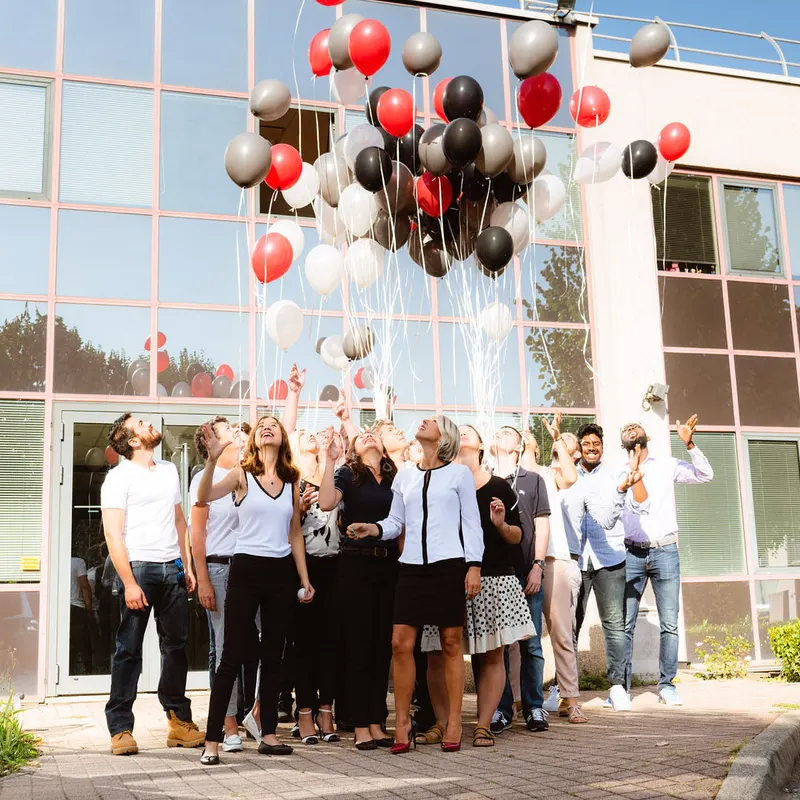 Équipe d’entreprise lançant des ballons devant ses locaux à Lyon, visages levés vers le ciel