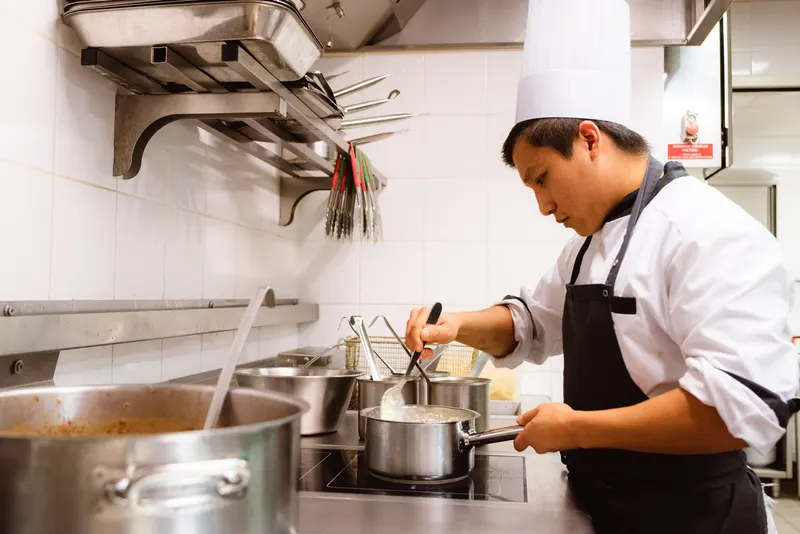 Cuisinier en tenue blanche remuant une sauce dans une cuisine professionnelle