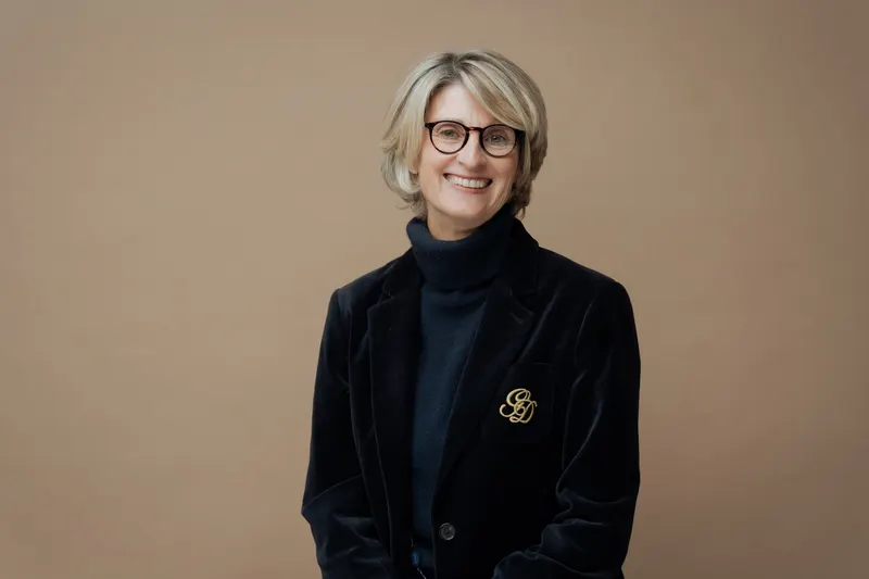 Portrait d’une femme souriante à lunettes, veste en velours, fond beige