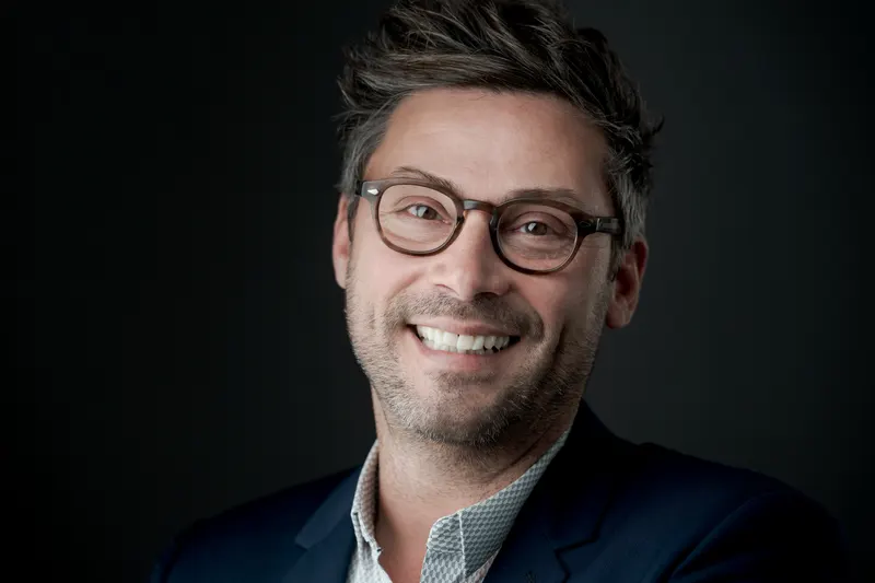 Portrait d’un homme à lunettes au grand sourire, fond sombre