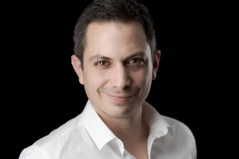 Portrait d’un homme en chemise blanche, sourire en coin, fond noir