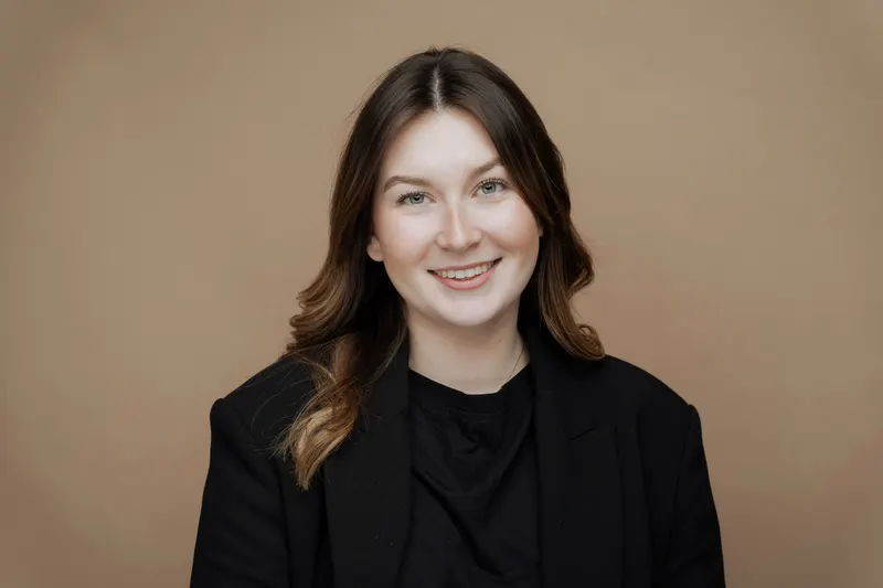 Portrait d’une jeune femme souriante en blazer noir, fond brun clair