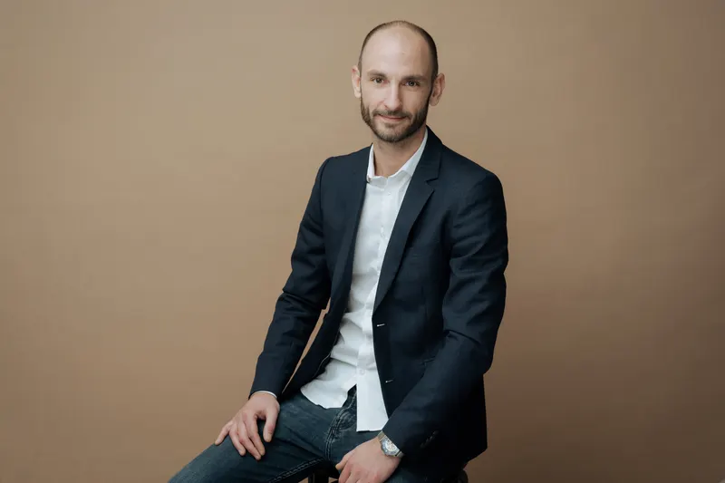 Portrait d’un homme assis en veste bleu marine, regard direct, fond beige