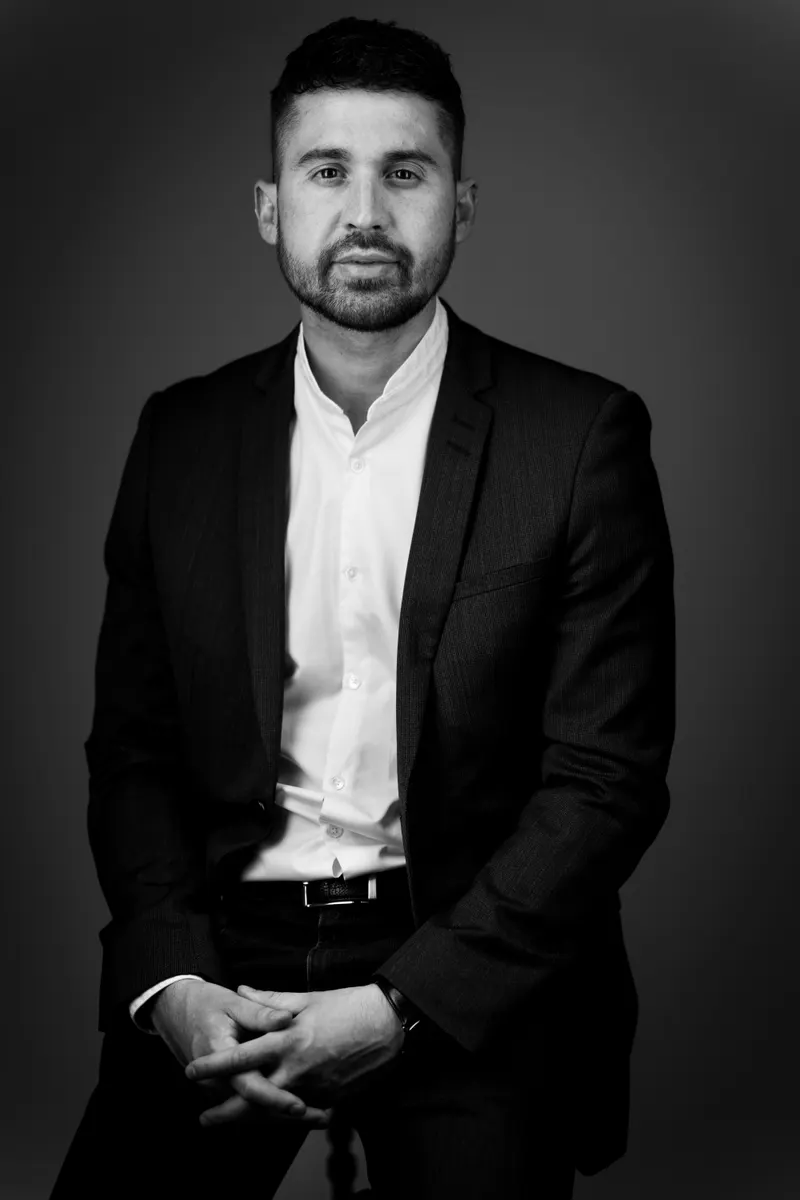 Portrait en noir et blanc d’un homme en costume, les mains jointes
